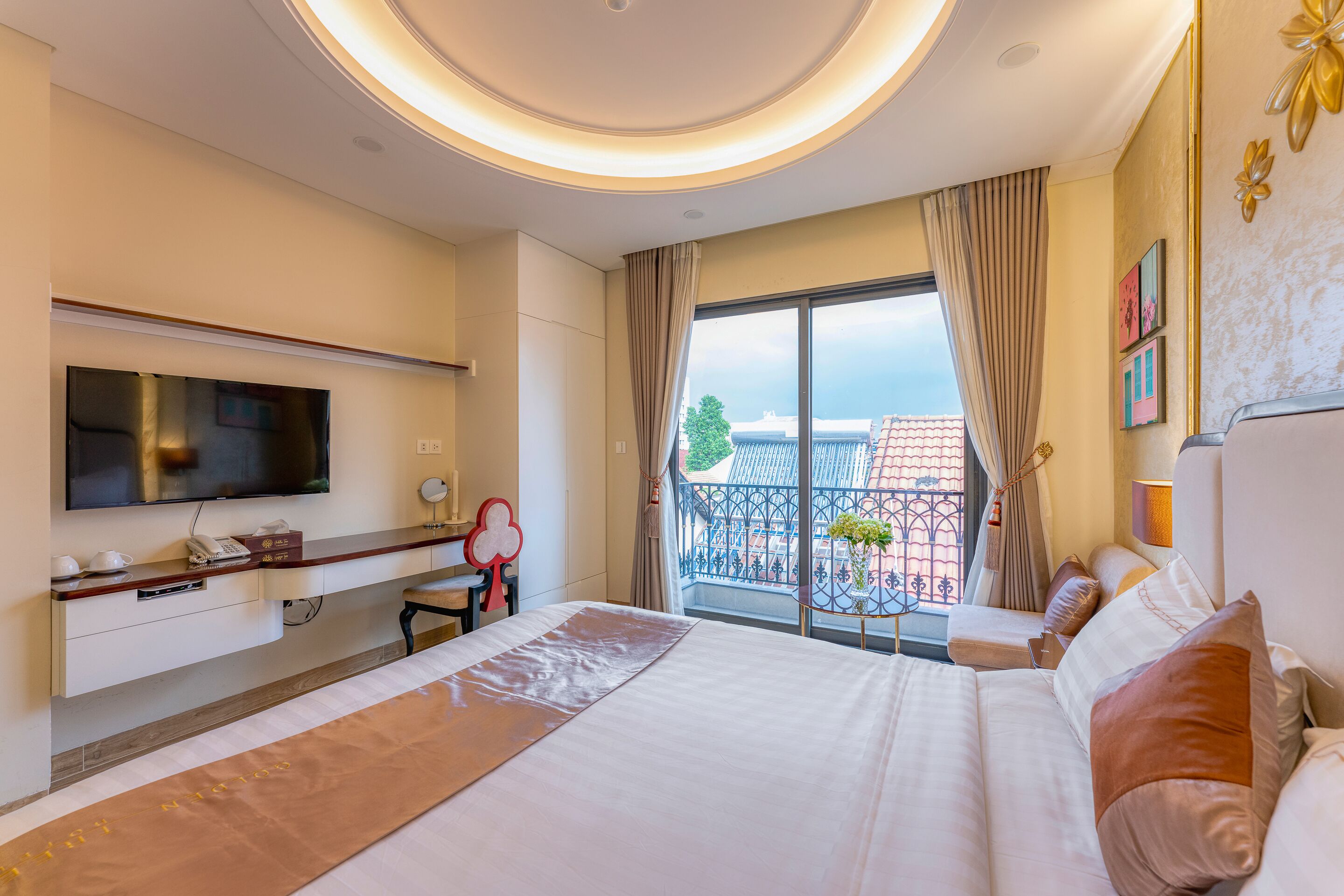 A hotel room with a bed, a desk, a TV, and a balcony with a view of buildings.
