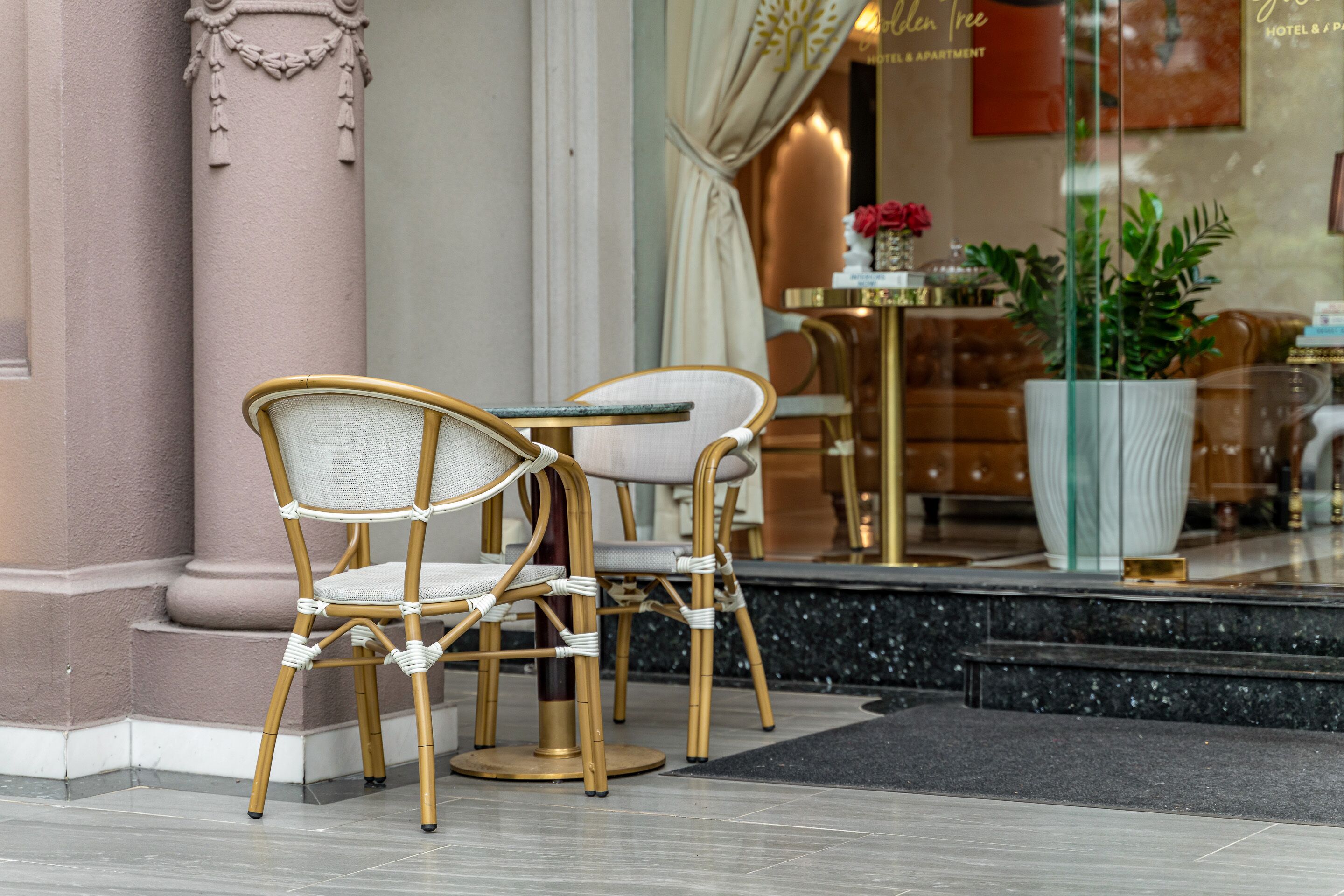 A hotel lobby with two wicker chairs, a marble floor, and a large potted plant.