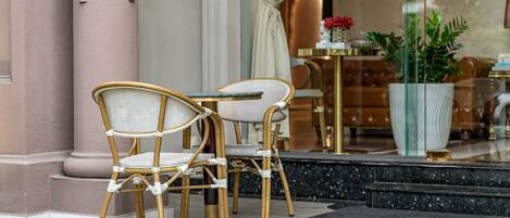 A hotel lobby with two wicker chairs, a marble floor, and a large potted plant.