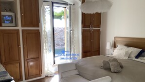 A bedroom with a bed, a chair, wooden cabinets, and a view of the outside. - Les Grimaldines - Maison d'Hotes C 2 Bis (Cagnes-sur-Mer)