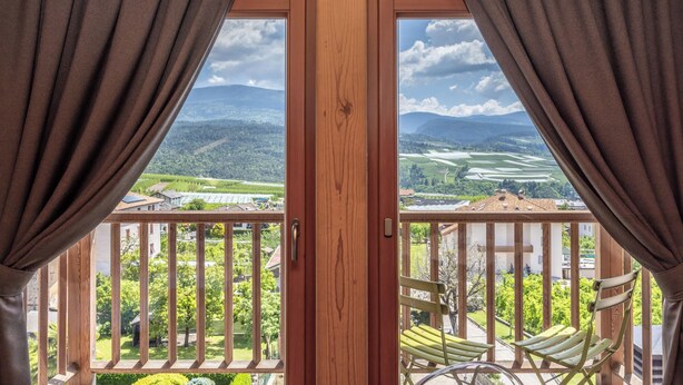 A balcony with a wooden railing, a view of a green landscape, and a door with curtains. - Horse House (Novella)