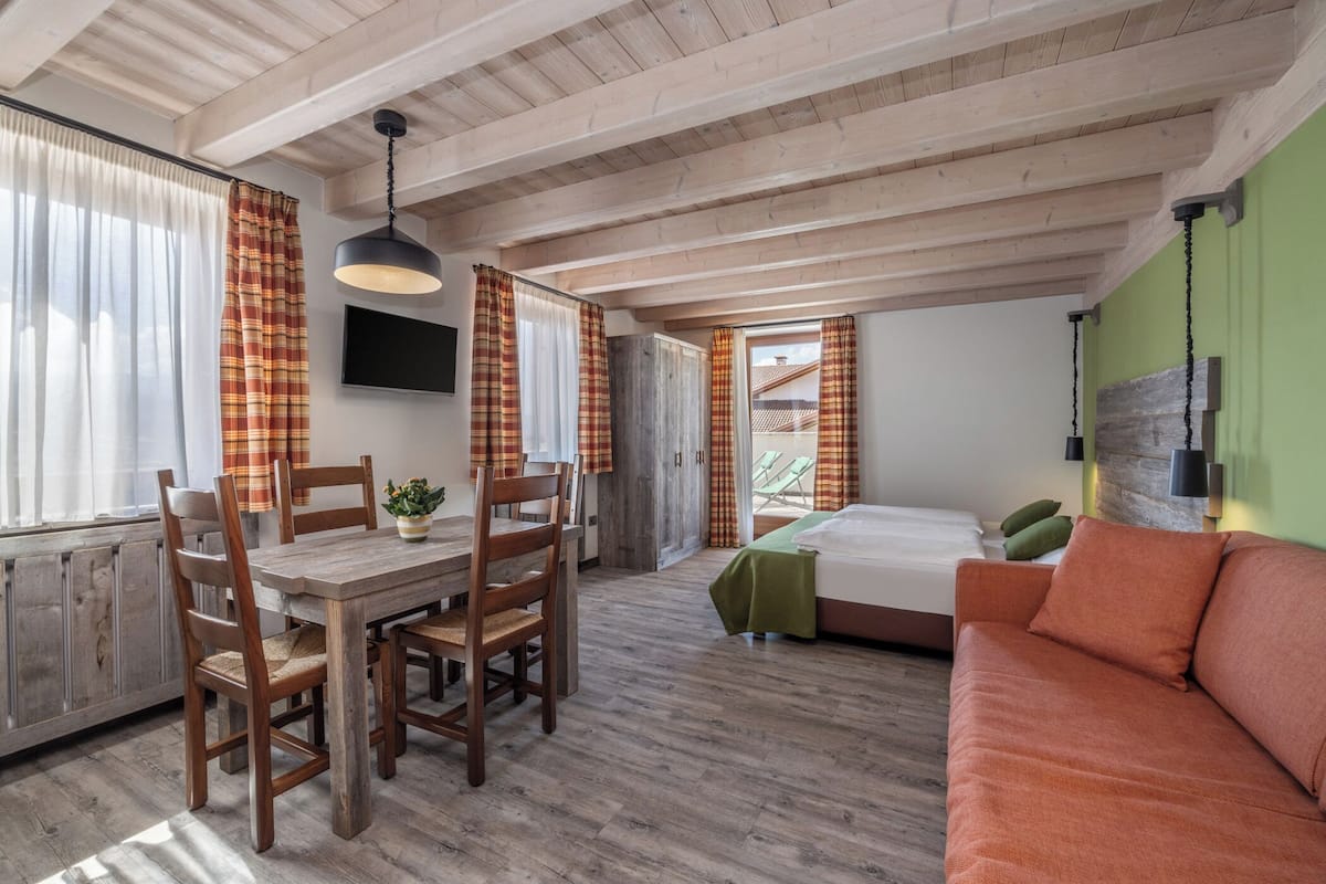 A cozy room with a wooden dining table, chairs, a sofa, and a bed.