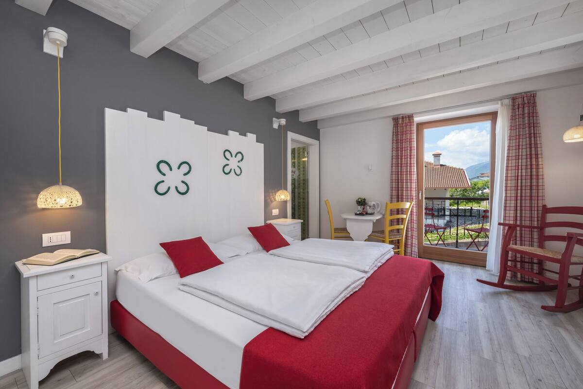 A bedroom with a double bed, a nightstand, a lamp, a chair, and a view of the outdoors.
