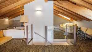 An attic bedroom with a glass door leading to a living area, a bathtub, and a wheelchair. - Horse House (Novella)