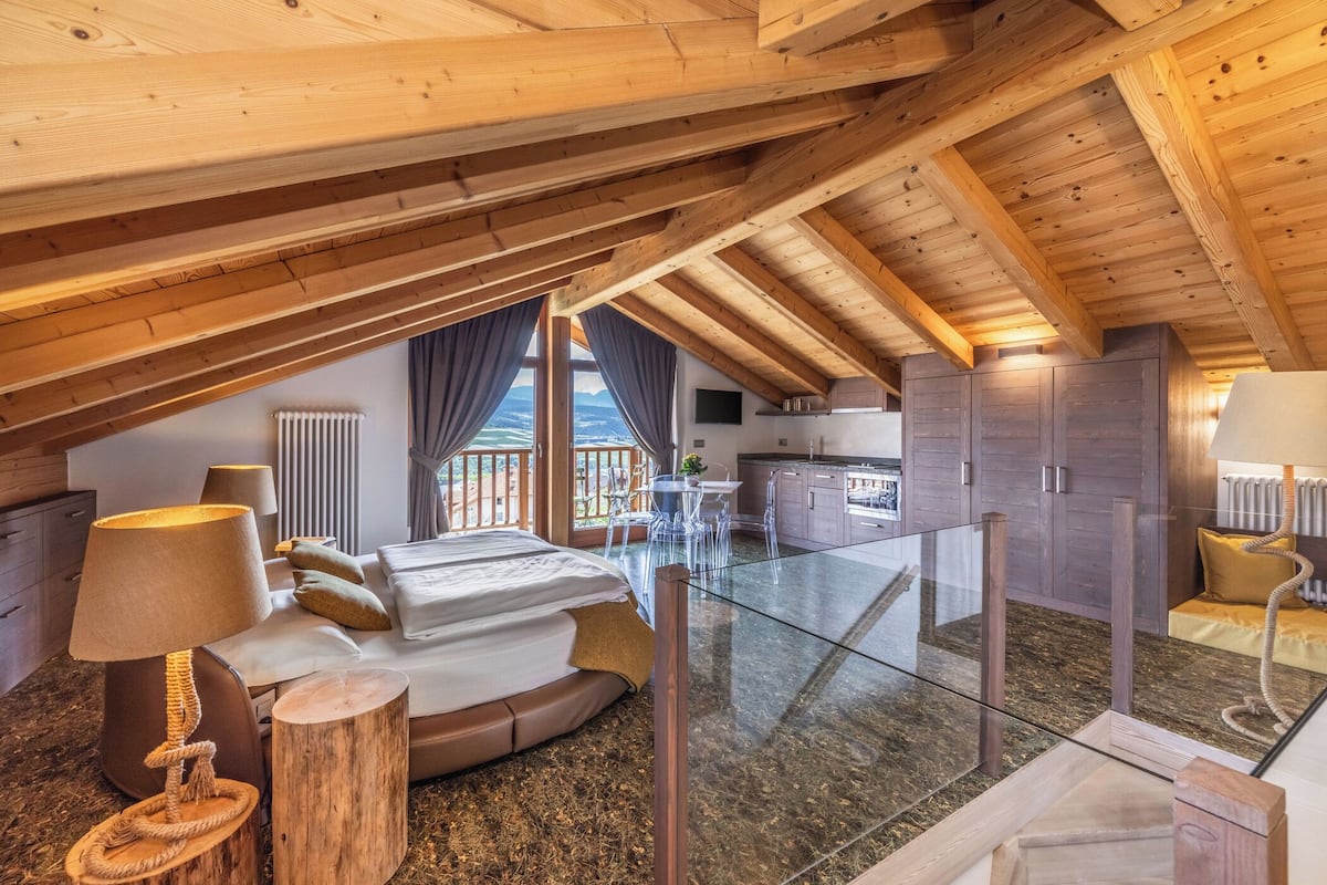 A high-ceilinged room with a glass floor, wooden beams, a bed, a table, and a kitchen area.