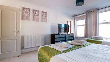 A bedroom with two beds, a dresser, a TV, and a window with curtains.