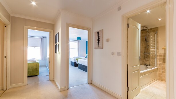 A hallway leading to a bedroom with a bed and a bathroom with a shower. - Old Town Central Apartments (Swindon)