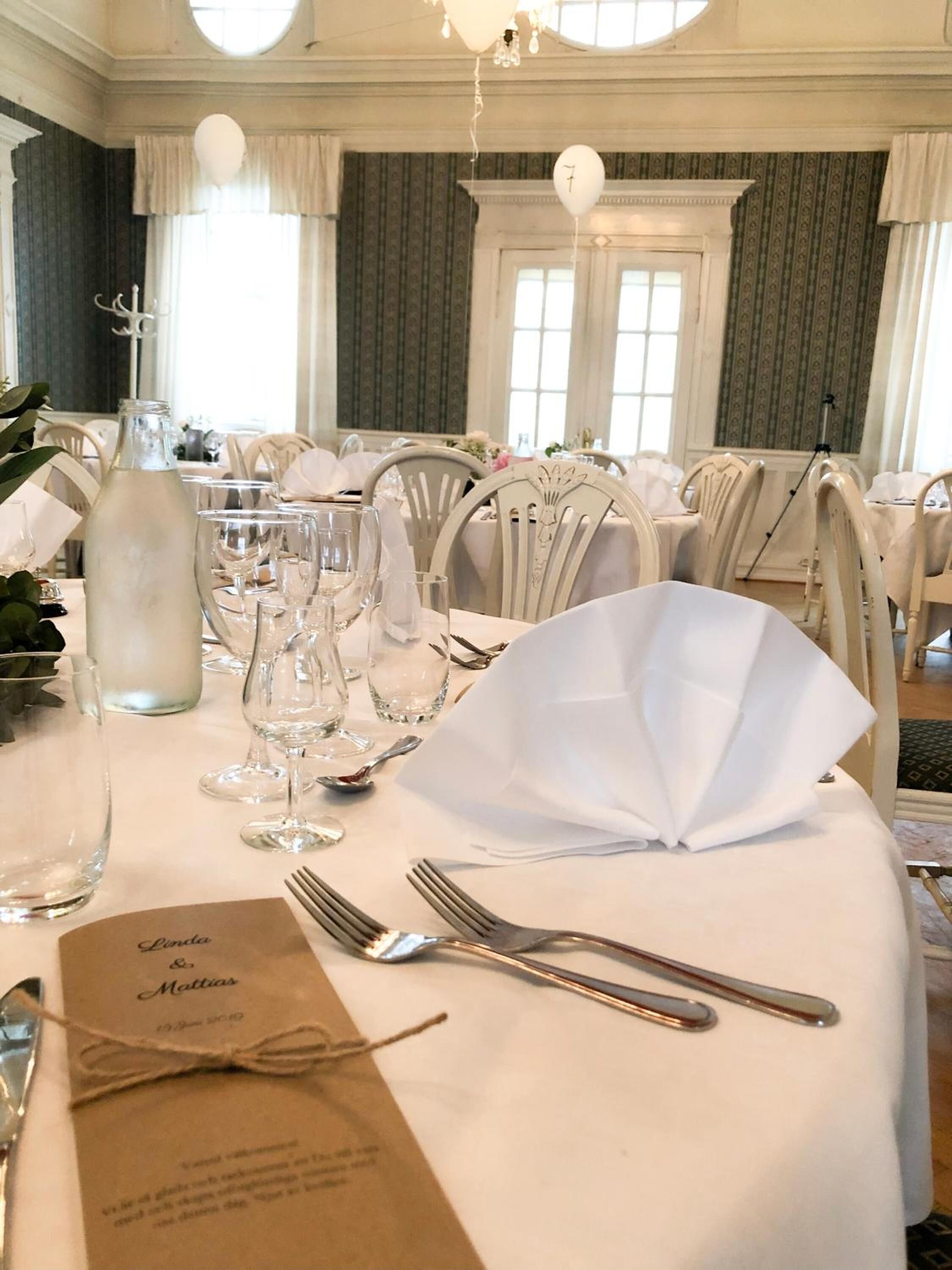 Mesa de jantar posta para uma recepção de casamento, com toalhas brancas, copos e cartão de menu.
