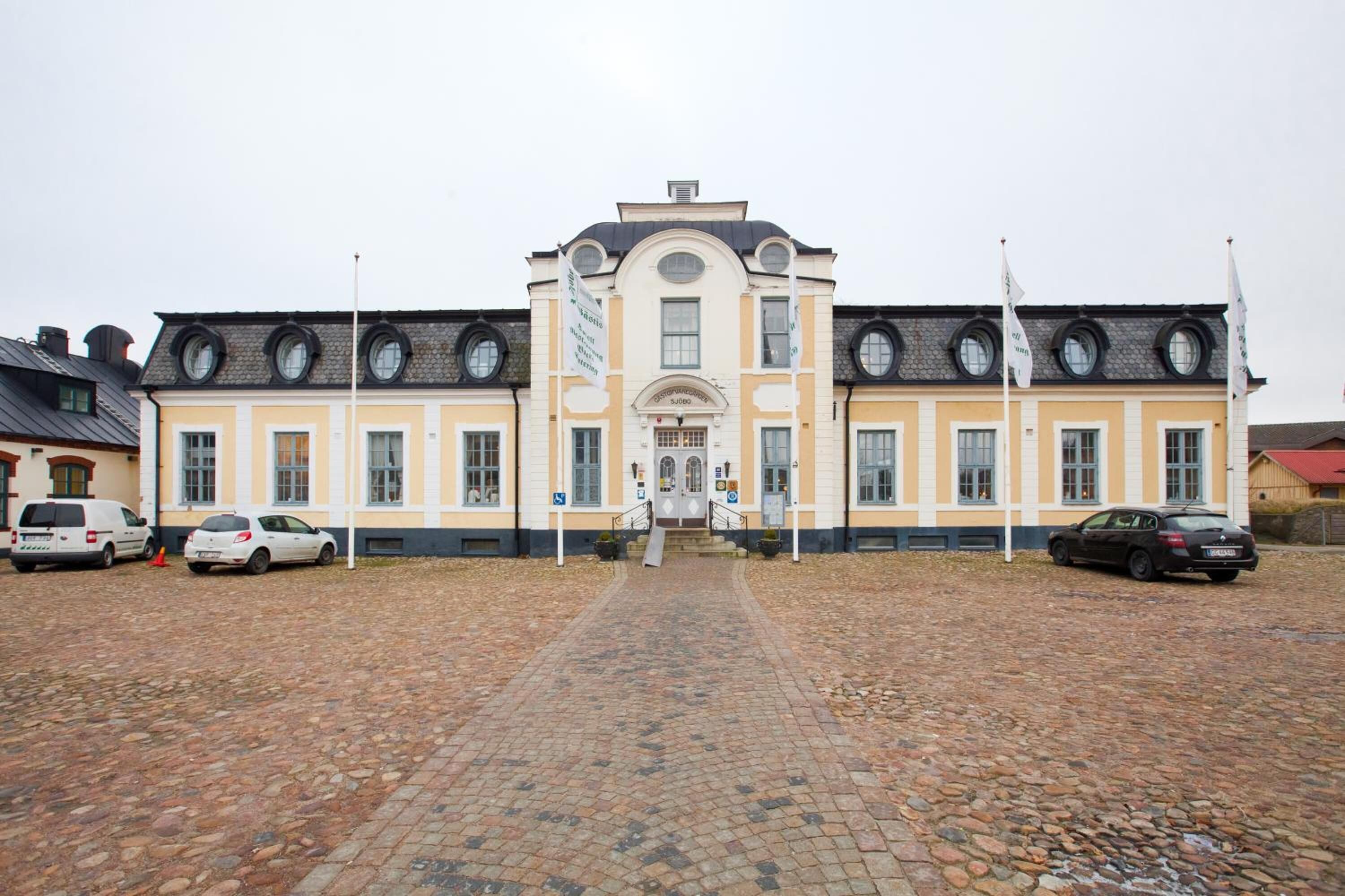 Un bâtiment historique doté d’une entrée centrale, de nombreuses fenêtres et d’une cour pavée.
