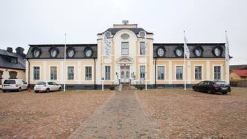 Un bâtiment historique doté d’une entrée centrale, de nombreuses fenêtres et d’une cour pavée.