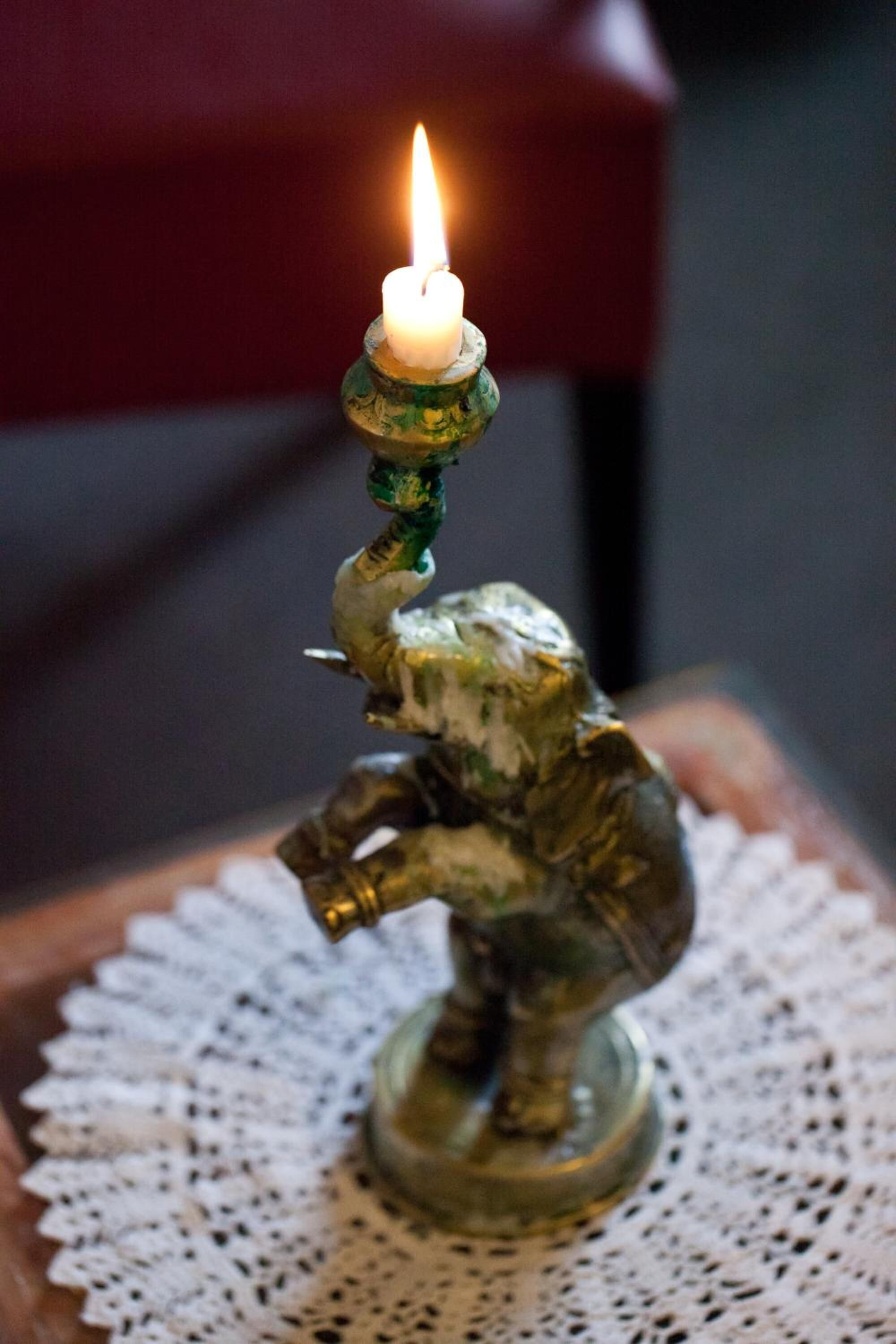 A small, ornate candle holder with a lit candle on a lace doily.