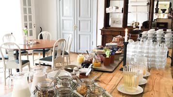 Ein Essbereich mit einem langen Holztisch, gedeckt für das Frühstück, mit Gläsern voller Brotaufstriche, einer Milchkanne und verschiedenen Frühstücksangeboten.