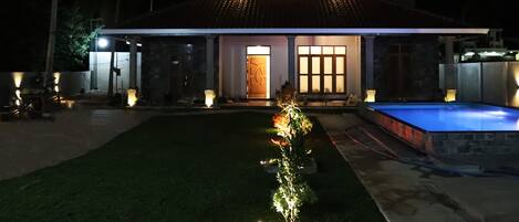 Een modern huis met een zwembad, een goed verlichte entree en een keurig onderhouden gazon.