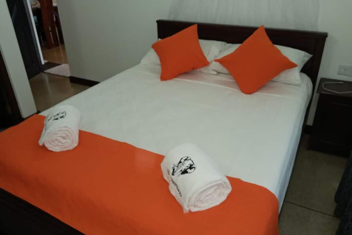 Una cama bien hecha con ropa blanca y almohadas naranjas, una toalla enrollada sobre la cama y un cabecero de madera.