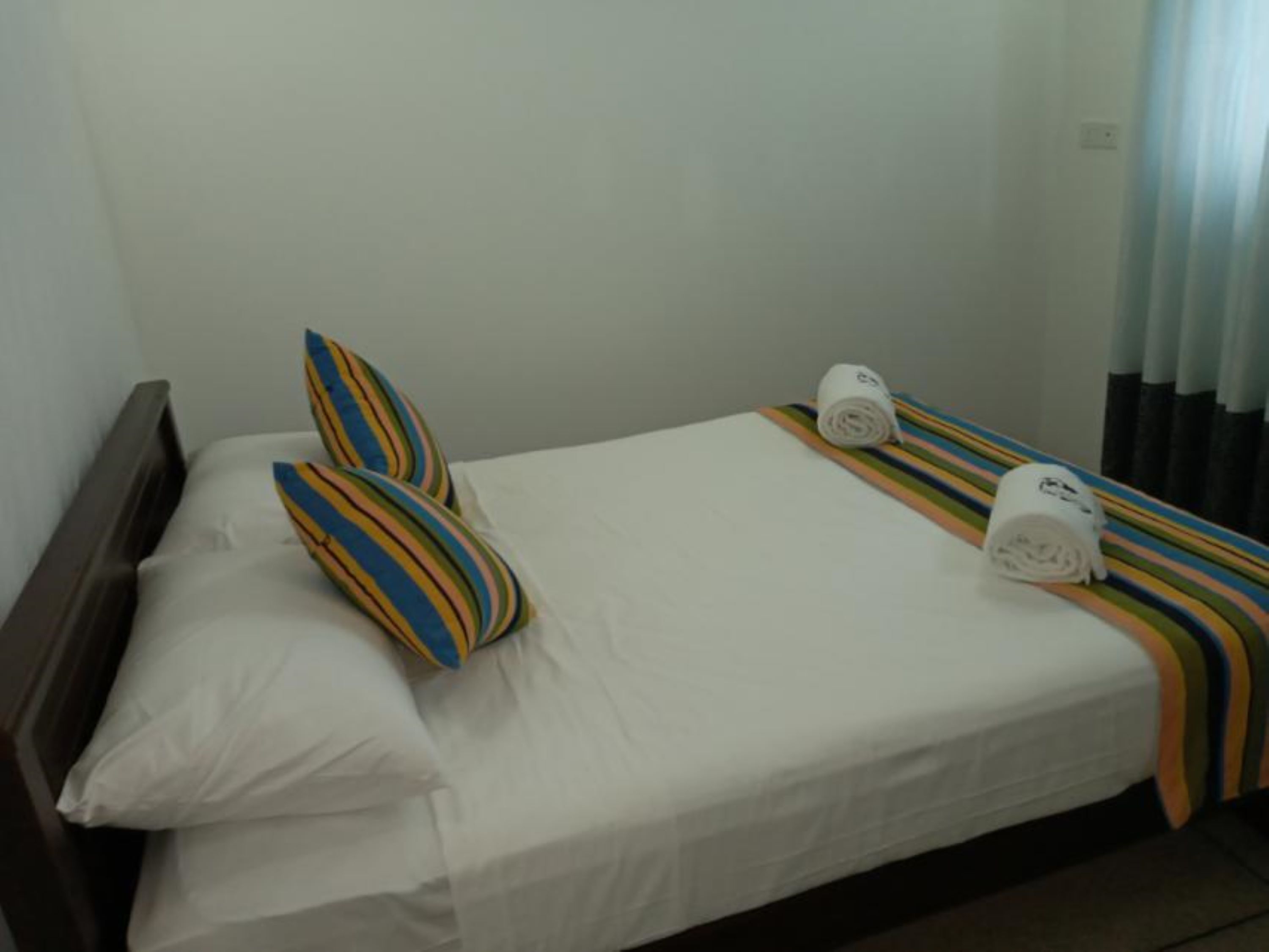 A single bed with white bedding, two striped pillows, a striped blanket, and two white towels on the bed.
