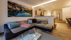 A modern living room with a sectional sofa, a glass coffee table, and a large landscape painting. - Apartment Goldeck (Ried im Oberinntal)