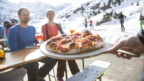 A pizza on a wooden board held by a person. - Apartment Goldeck (Ried im Oberinntal)
