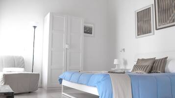 A bedroom with a bed, a chair, a wardrobe, a bedside table with a lamp, and a picture on the wall.