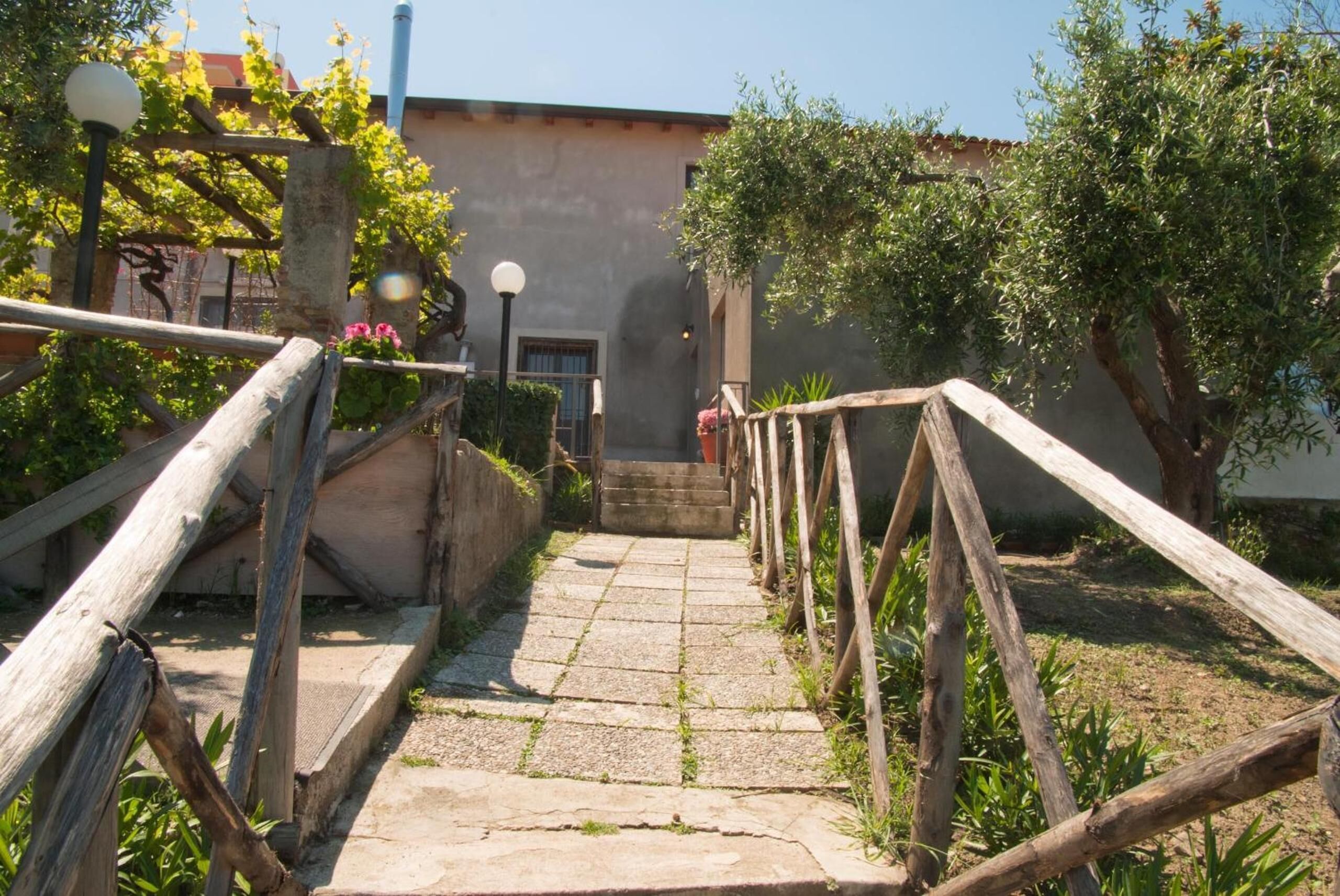 Un sentiero in pietra conduce a un edificio con un recinto rustico in legno e vegetazione.