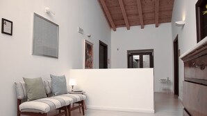 A modern living room with a wooden bench, a white sofa, and a small table with a lamp. There are framed artworks on the walls and a wooden cabinet. - Bookbreakfast (Terme Vigliatore)