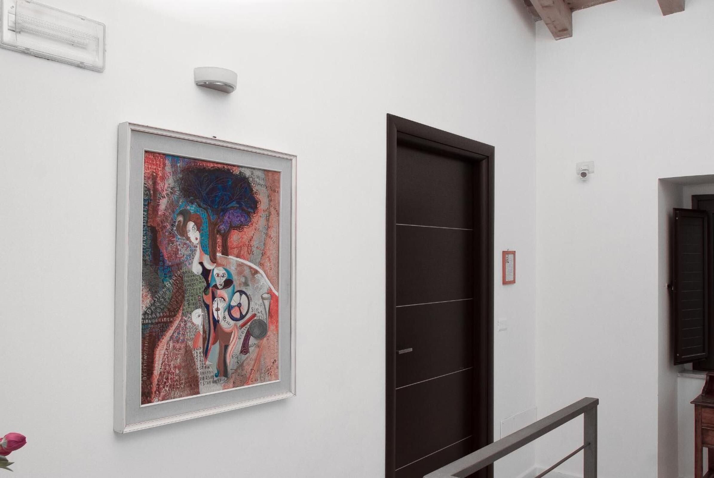 A hallway with a framed abstract painting, a dark door, and a white wall.
