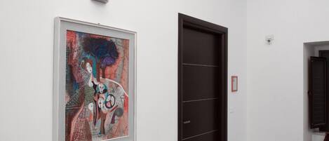 A hallway with a framed abstract painting, a dark door, and a white wall.