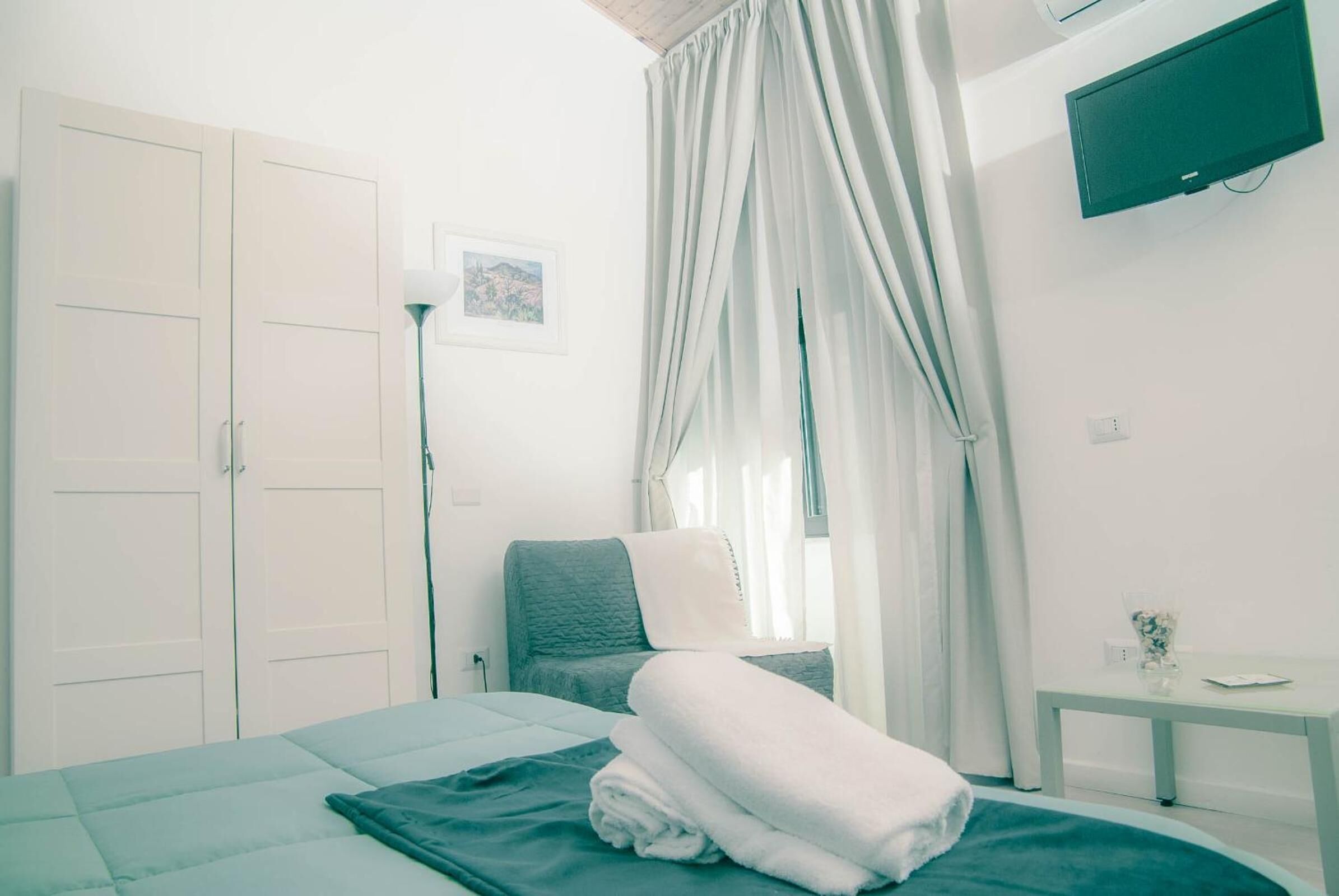 Una camera da letto con un letto, un comodino, una TV, un armadio e una finestra con tende.