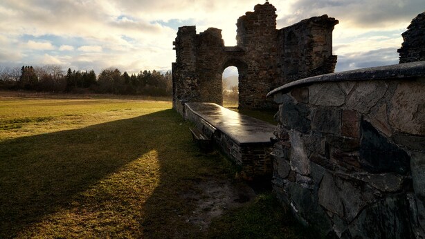 An ancient stone structure with a large archway, surrounded by a grassy field and a stone wall. - Klostergården Tautra (Frosta)