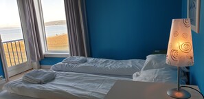 A hotel room with a bed, a bedside lamp, a window with curtains, and a view of the sea. - Klostergården Tautra (Frosta)
