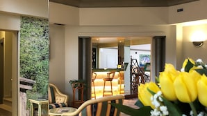 A hotel lobby with a patterned floor, a seating area with striped chairs, a table with a glass top, and a yellow flower arrangement. - Crystal Hotel Varese (Varese)