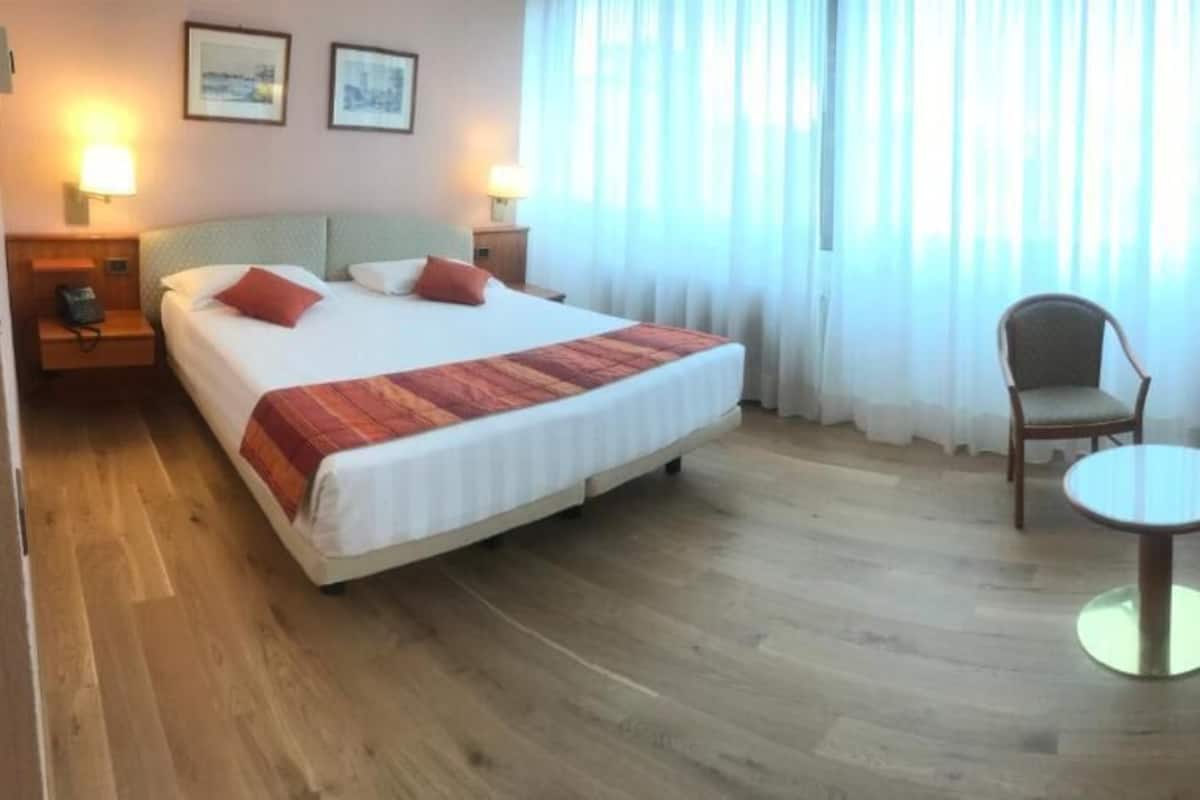 A hotel room with a bed, a chair, a small table, and a desk.