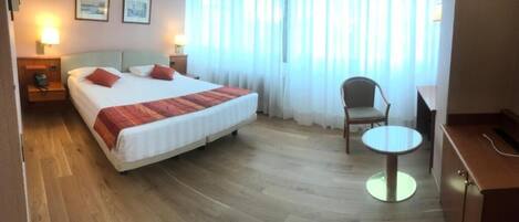 Una habitación de hotel con una cama, una silla, una mesita y un escritorio.