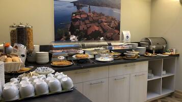 Montaje de bufé con diferentes opciones de comida y una máquina de café, un cartel con una vista panorámica, y platos y tazas ordenados.