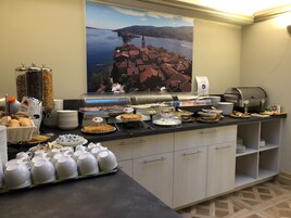 Montaje de bufé con diferentes opciones de comida y una máquina de café, un cartel con una vista panorámica, y platos y tazas ordenados.