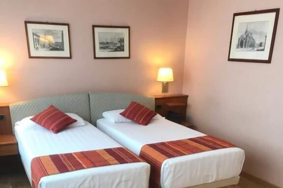 A hotel room with two single beds, a sofa, a small table, and framed pictures on the wall.
