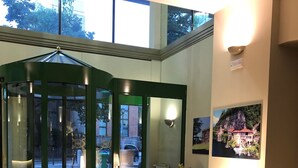 A lobby with a revolving door, yellow armchairs, a glass table, and a framed picture on the wall. - Crystal Hotel Varese (Varese)