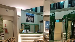 A lobby with a reception desk, patterned carpet, and striped armchairs. - Crystal Hotel Varese (Varese)