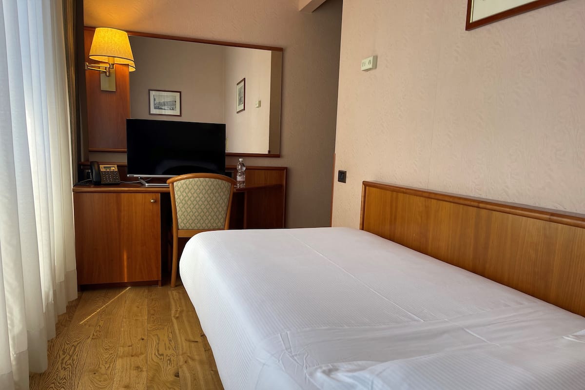 A hotel room with a bed, a desk with a telephone, a chair, a television, and a lamp.