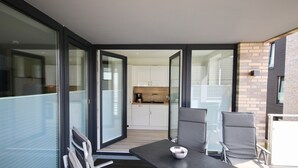 Una cocina moderna con armarios blancos y encimera negra. Hay una zona de comedor con dos sillas grises y una mesa.