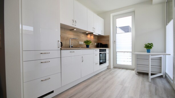Una cocina moderna con armarios blancos, horno integrado y ventana que proporciona luz natural.