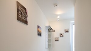 Un pasillo con suelo de madera, un banco blanco y un perchero en la pared.