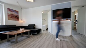 Una sala de estar moderna con un sofá negro, una mesa de centro de madera y un televisor de pantalla plana montado en la pared.