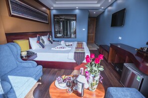 A hotel room with a bed, a sofa, a dining table with a bottle of wine, glasses, and a vase of flowers. - Sapa Full House Hotel (Sa Pa)