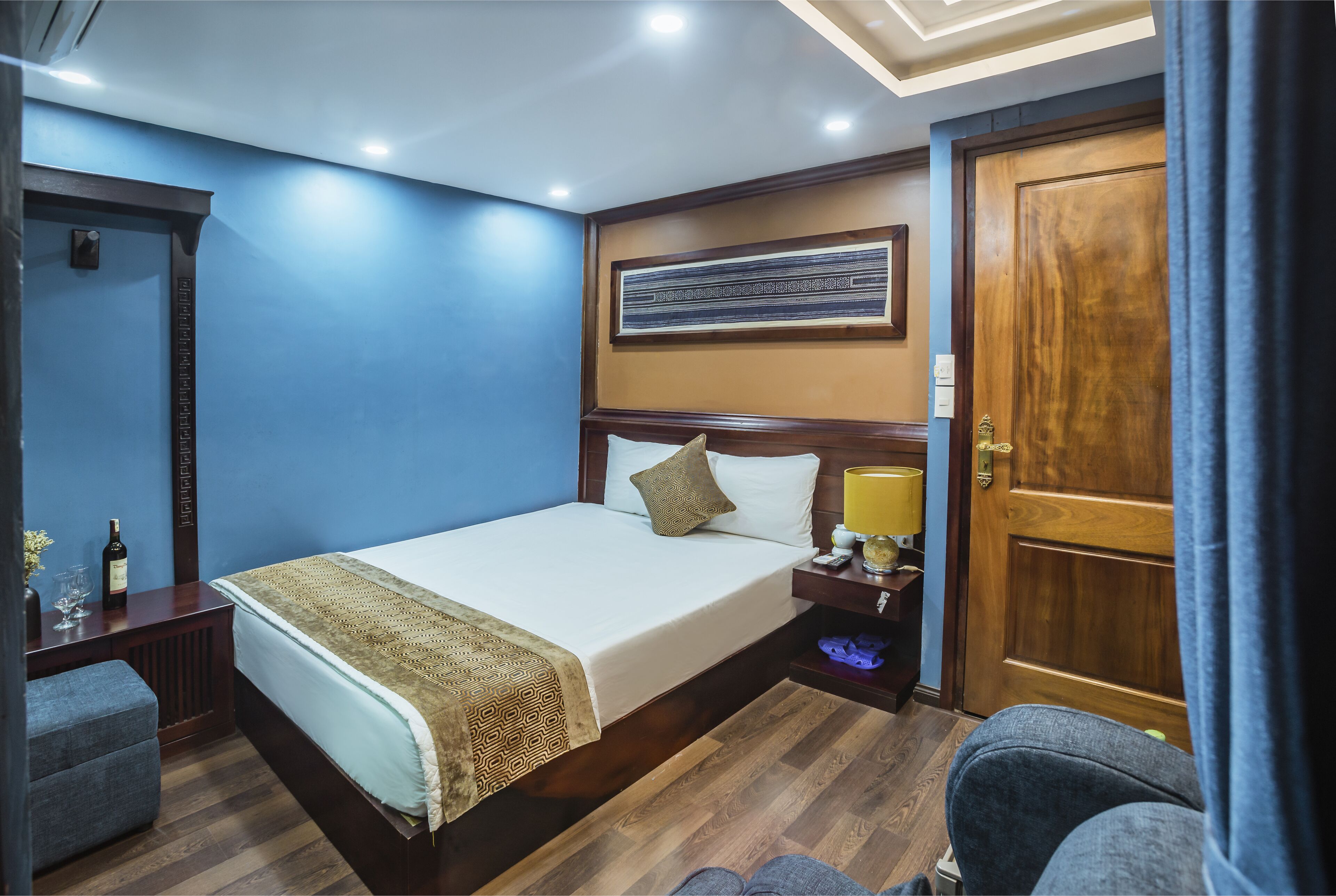 A hotel room with a large bed, a nightstand, a lamp, and a wooden door.