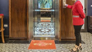 A woman in a red jacket standing in front of an elevator with a patterned floor and a red mat. - Sapa Full House Hotel (Sa Pa)
