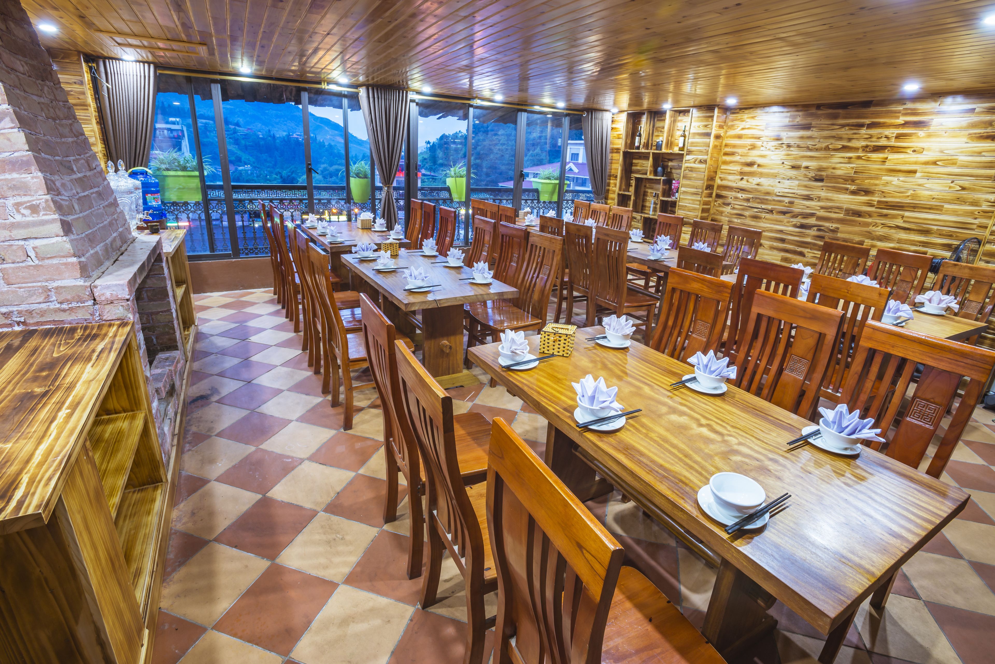 A restaurant with wooden tables and chairs, a brick fireplace, and large windows with a view of the mountains.