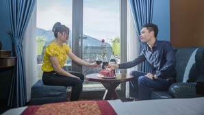 A room with a large window, a sofa, a small table with a plate of fruit, and a bed with a red and yellow bedspread. - Sapa Full House Hotel (Sa Pa)