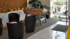 Un vestíbulo moderno con una mesa de fútbol de mesa, sillas de cuero negro y una variedad de plantas en macetas.