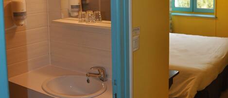 A bathroom with a sink, mirror, and hand dryer. There is a window with a view of greenery outside.
