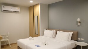Ein ordentlich bezogenes Bett mit weißen Leinentüchern, ein kleiner Nachttisch und eine Wand-Klimaanlage.